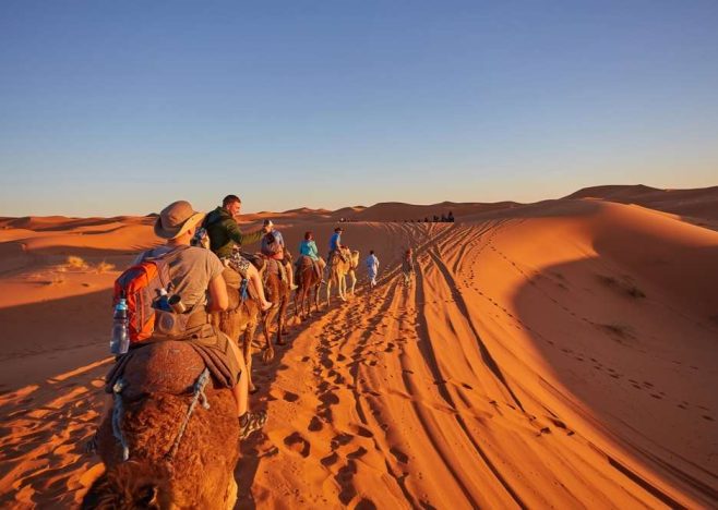 Tourists,Riding,Camels,,Smiling,,In,The,Sahara,Desert,,Morocco.